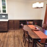 Open-plan dining area with a long wooden table, matching chairs, and orange striped runner under a modern pendant light.