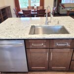 Kitchen island with a stainless steel sink and curved faucet, granite countertop, and dark wood cabinets underneath.