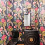 Small bathroom with bold tropical floral wallpaper, a gold-framed mirror, and a black vanity.