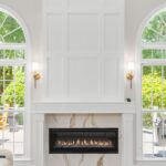 Bright living room with a tall white paneled wall above a marble fireplace, flanked by arched windows and wall sconces.